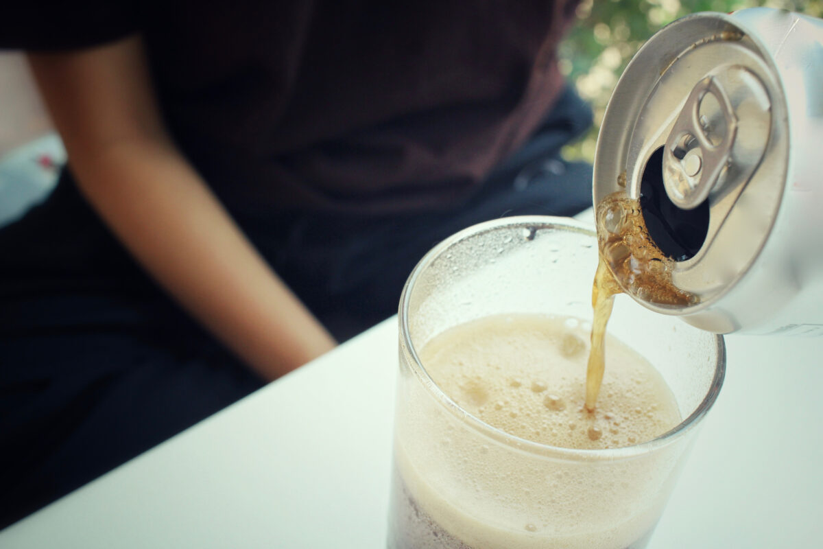 Cola being poured from a can into a glass filled with ice