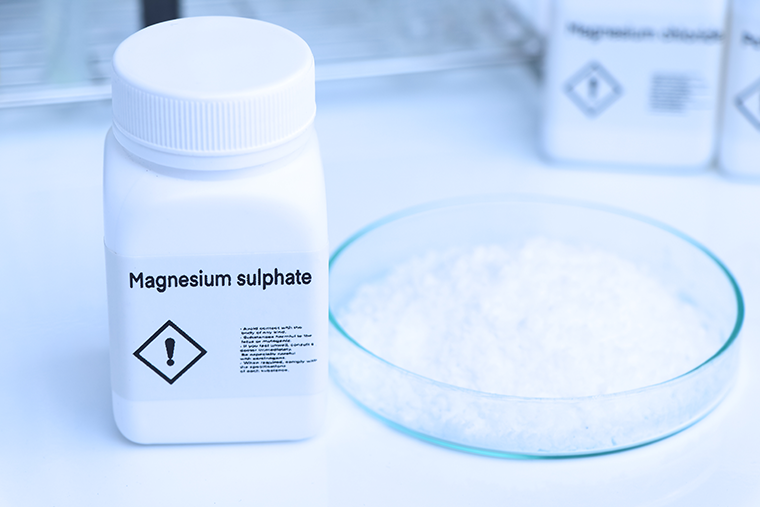 Labelled bottle of magnesium sulfate next to a dish of magnesium sulphate in white powder form