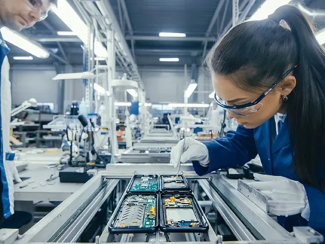 An electronics factory worker installing an electronic circuit on a production line