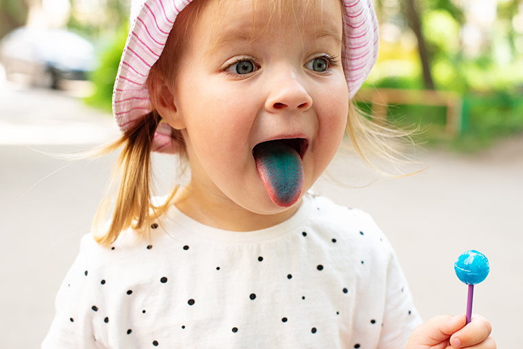 Young girl eating a blue lollypop and sticking out her blue tongue