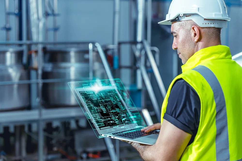 Engineer using AI software on a laptop in a factory