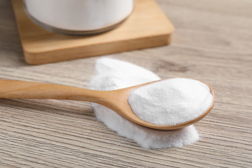 A wooden spoon filled with baking soda, spilled onto a wooden table.