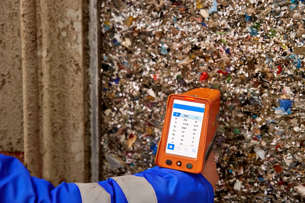 A worker in a blue hi-vis jacket uses an XRF scanner to check through rubbish for metals and other materials.