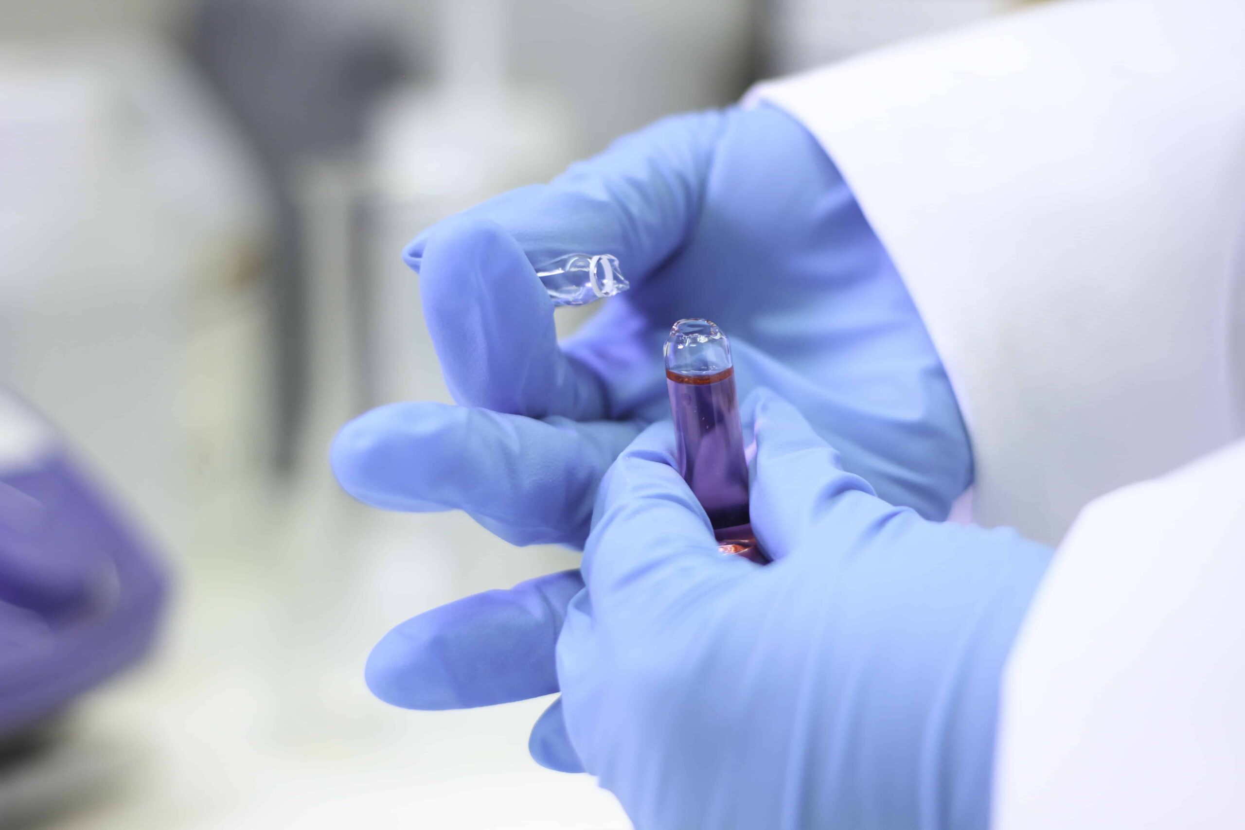 Close up of scientist wearing blue gloves holding a vial of chemicals