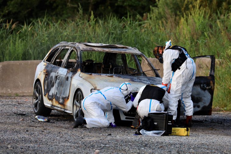 Forensic scientists examining a burnt out car