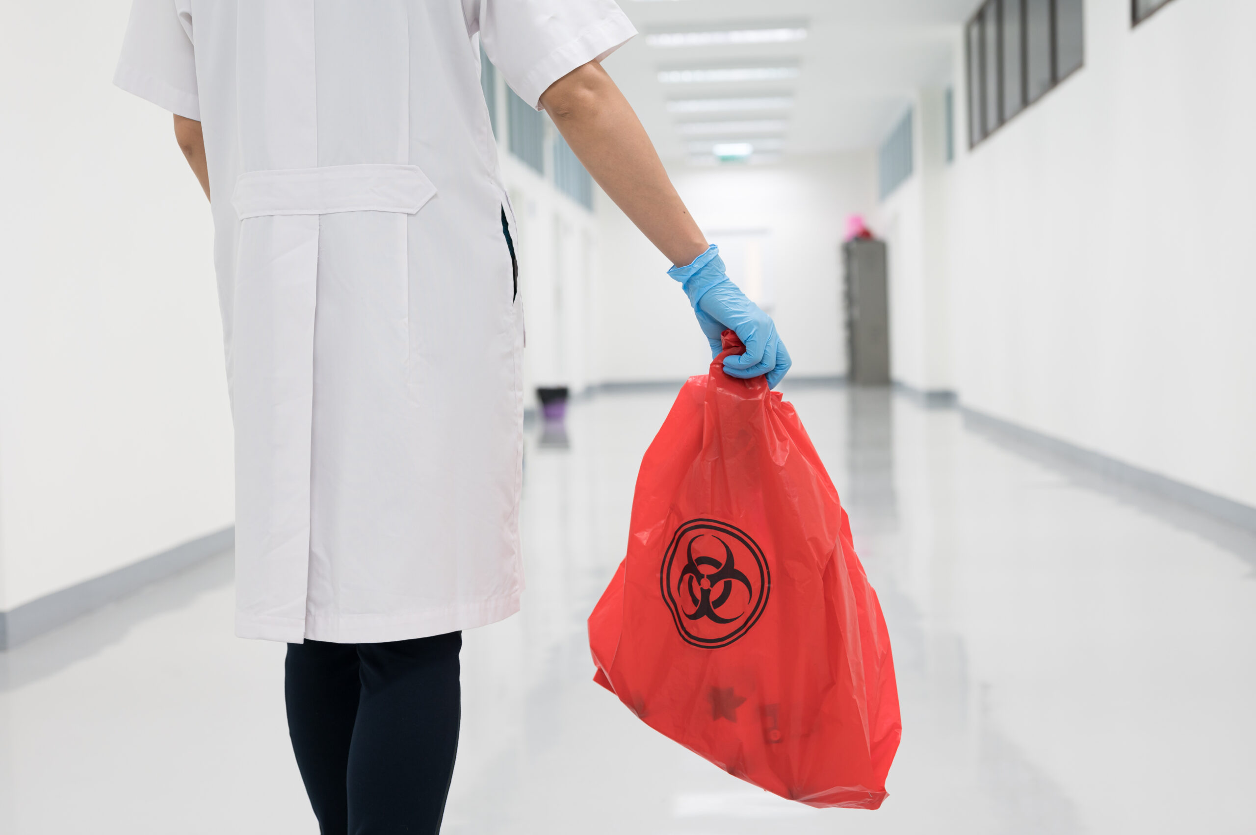 Scientist wearing blue gloves carrying a red plastic bag with a public biohazard sign.