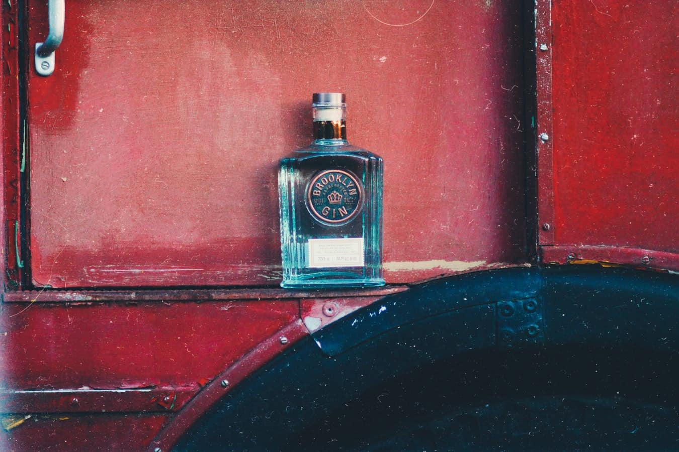 A square blue glass bottle of gin against a red wall