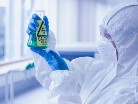 Close-up side view of a scientist in protective suit looking at hazardous blue chemical||Flammable chemicals in protection cabinet||Chemical hazard pictograms on test tubes||Close up of chemical bottle with toxic hazard label
