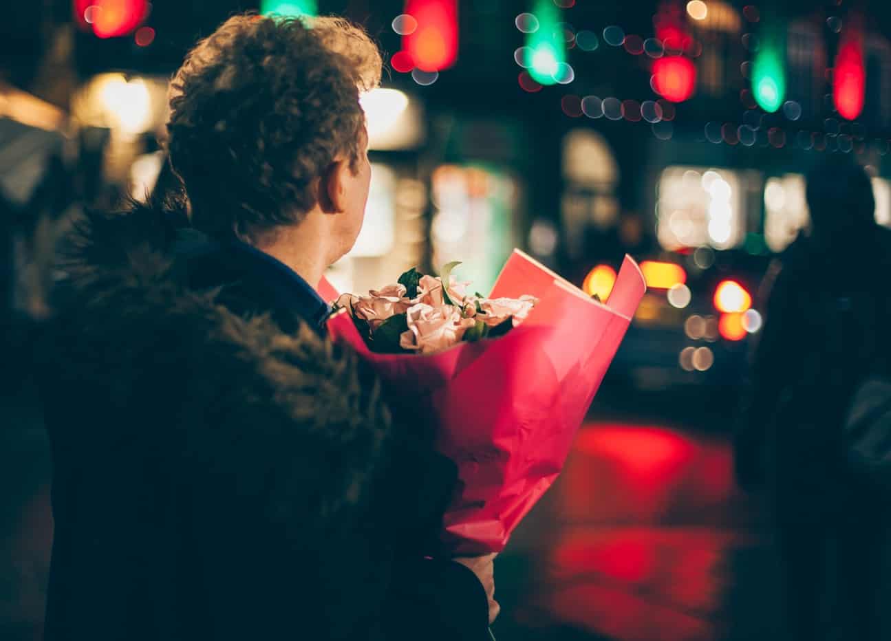 A man stood outside at night with a bouquet of flowers