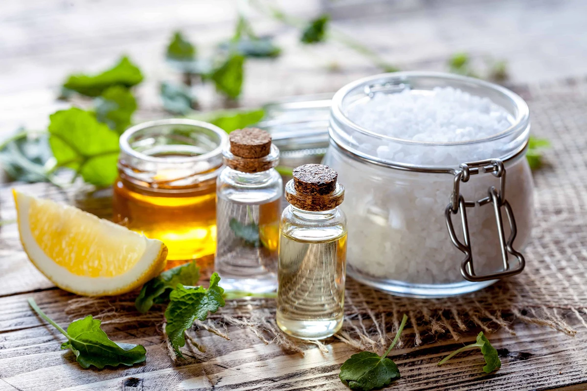 a lemon, olive oil, salt, and bottled liquids sit on a wooden surface with leaves draped about.