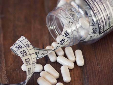 Thermogenic fat burners spilling out of pill bottle with measuring tape||Metabolism level scale with arrow||Coffee bean heart rate concept