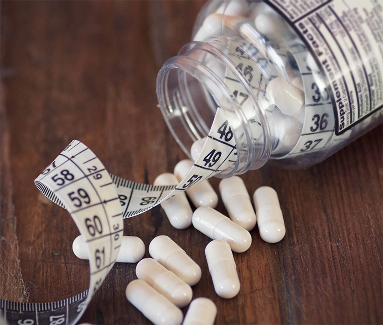 Thermogenic fat burners spilling out of pill bottle with measuring tape||Metabolism level scale with arrow||Coffee bean heart rate concept