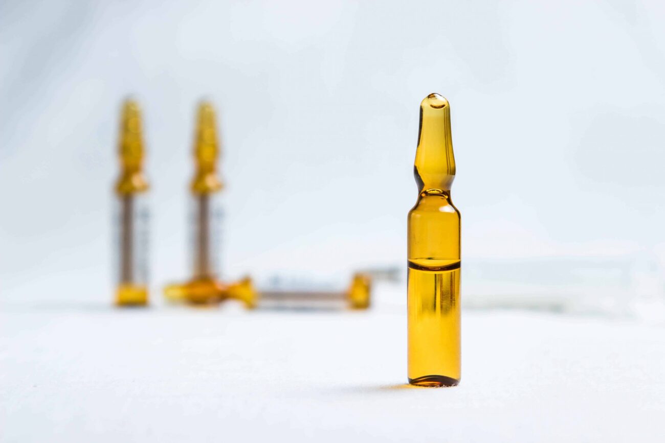 An ampoule with an injection is in the foreground. Behind