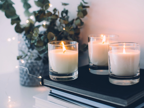 Three white vessel candles on a pile of books||Person holding a digital light lux meter to read the intensity of light||An infograogic explaining lumens and candelas