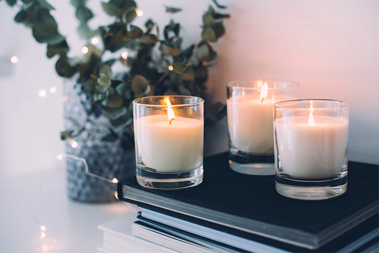 Three white vessel candles on a pile of books||Person holding a digital light lux meter to read the intensity of light||An infograogic explaining lumens and candelas
